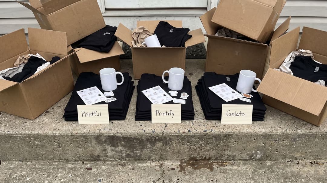 A low-angle view of a front step covered in delivery boxes and sample print-on-demand products, including t-shirts and mugs, labeled with handwritten index cards for comparison.
